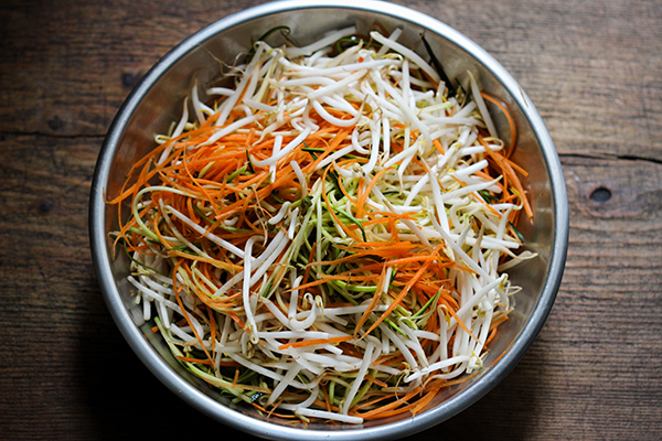 Zucchini- und Karottenstreifen mit Mungobohnen-Sprossen mischen
